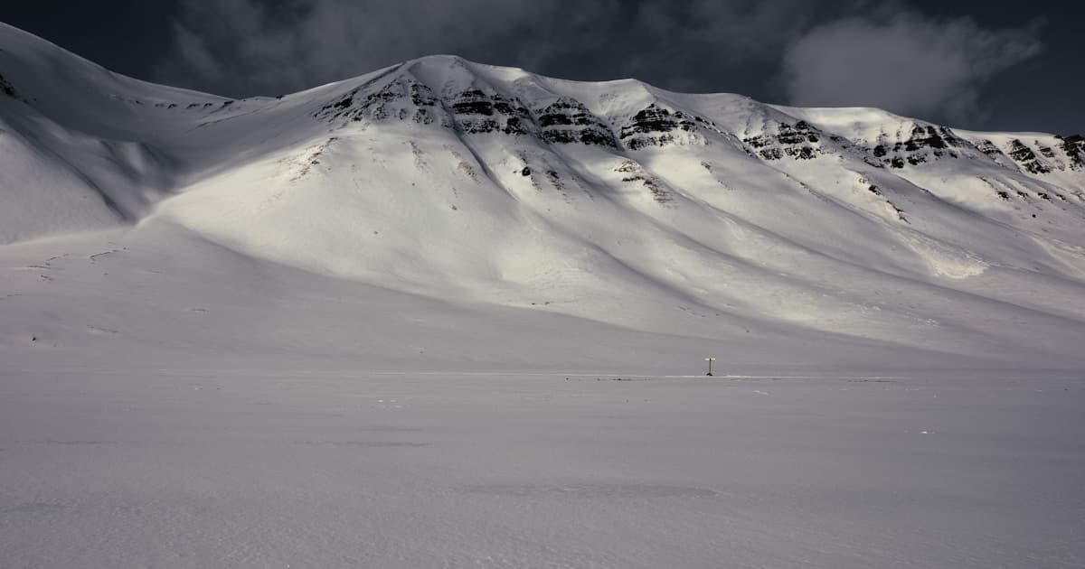 Snow-capped mountains rise above the blue Arctic sea in Svalbard