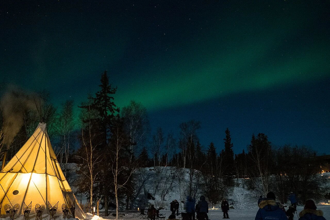 An aurora above a lit winter viewing area in Yellowknife