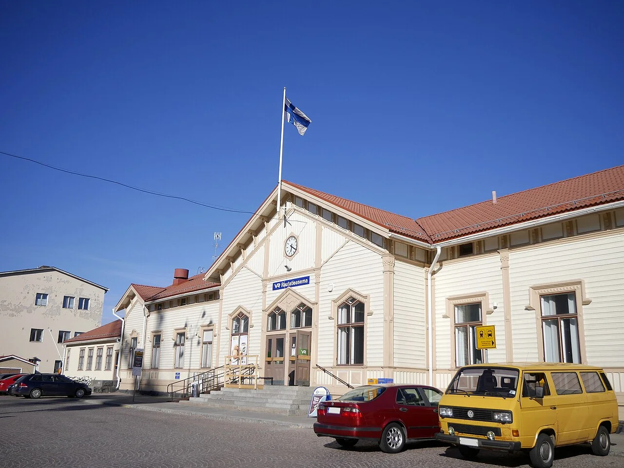 Cream-coloured Oulu railway station building with cars outside its entrance